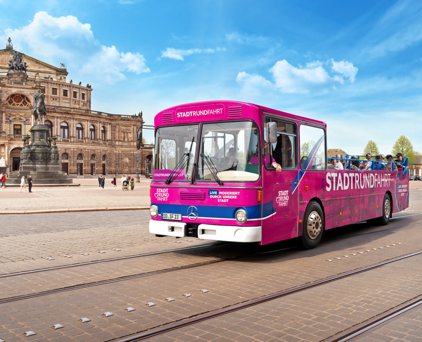 Ein pinker Stadtrundfahrt-Bus mit Gästen fährt an der Semperoper im Hintergrund vorbei, schönes Wetter