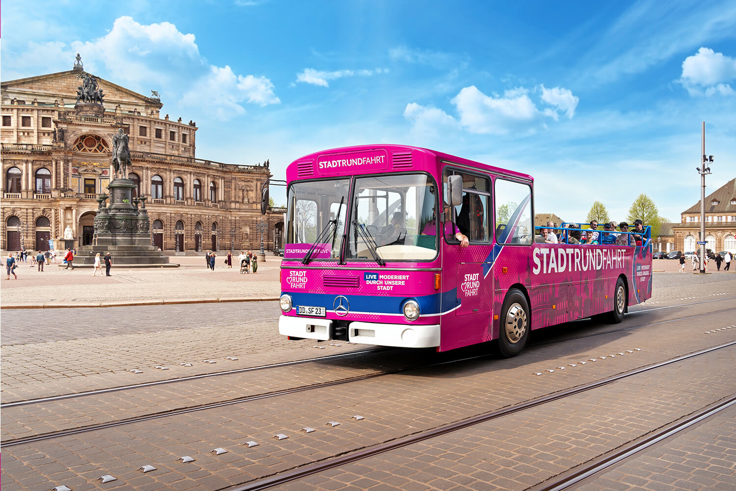 Ein pinker Stadtrundfahrt-Bus mit Gästen fährt an der Semperoper im Hintergrund vorbei, schönes Wetter