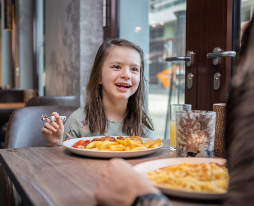 Mädchen sitzt lächelnd vor einem Teller Pommes