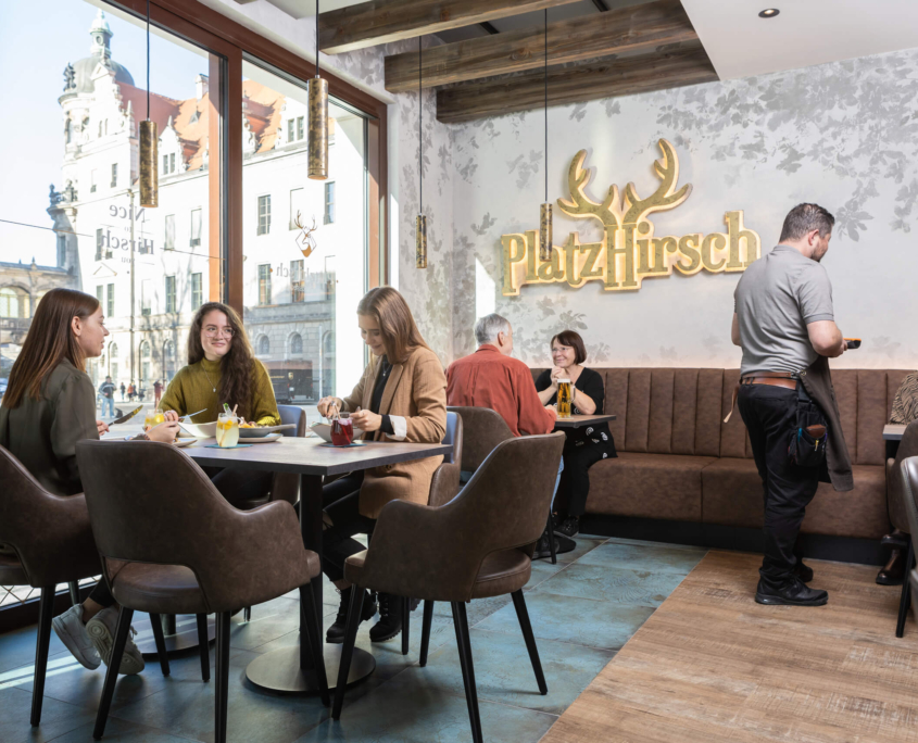 Gäste im Platzhirsch sitzen an Tischen, sehen fröhlich aus und werden von einem Kellner bedient