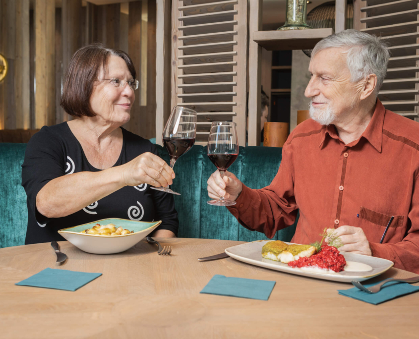 Ein älteres Pärchen sitzt an einem Tisch mit Essen und Getränken.
